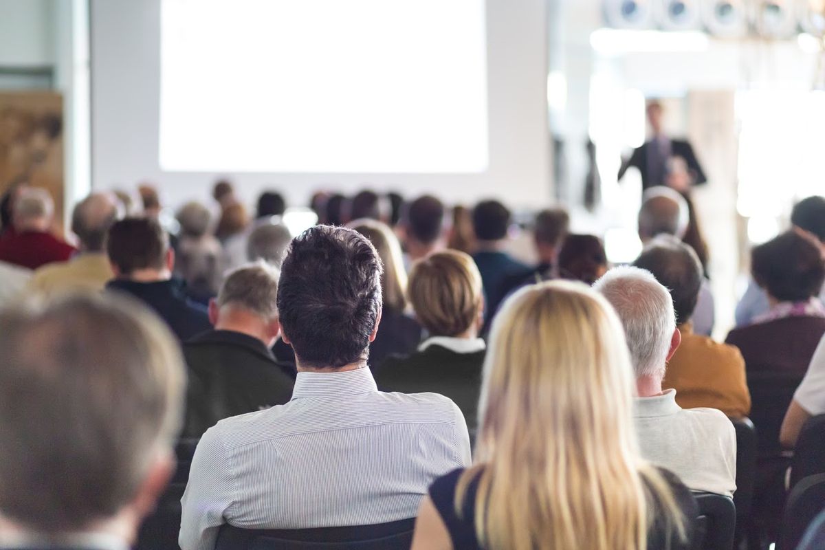 Audience sitting in formal attire attending a lecture with a slideshow presentation