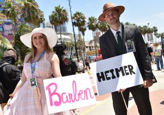 Cosplayers hold Barbenheimer signs outside the convention center during San Diego Comic-Con