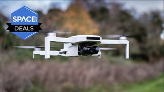 A white quadcopter drone is mid-flight in front of some trees and bushes with the space.com logo in the top left corner