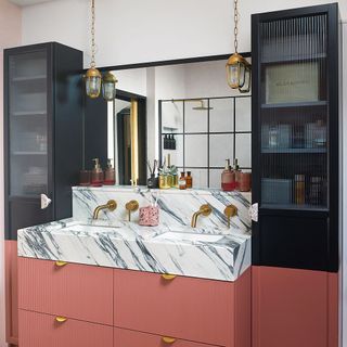 bathroom with pink painted cabinetry, fluted glass fronted cupboards, brass hardware, marble sink and pendant lighting