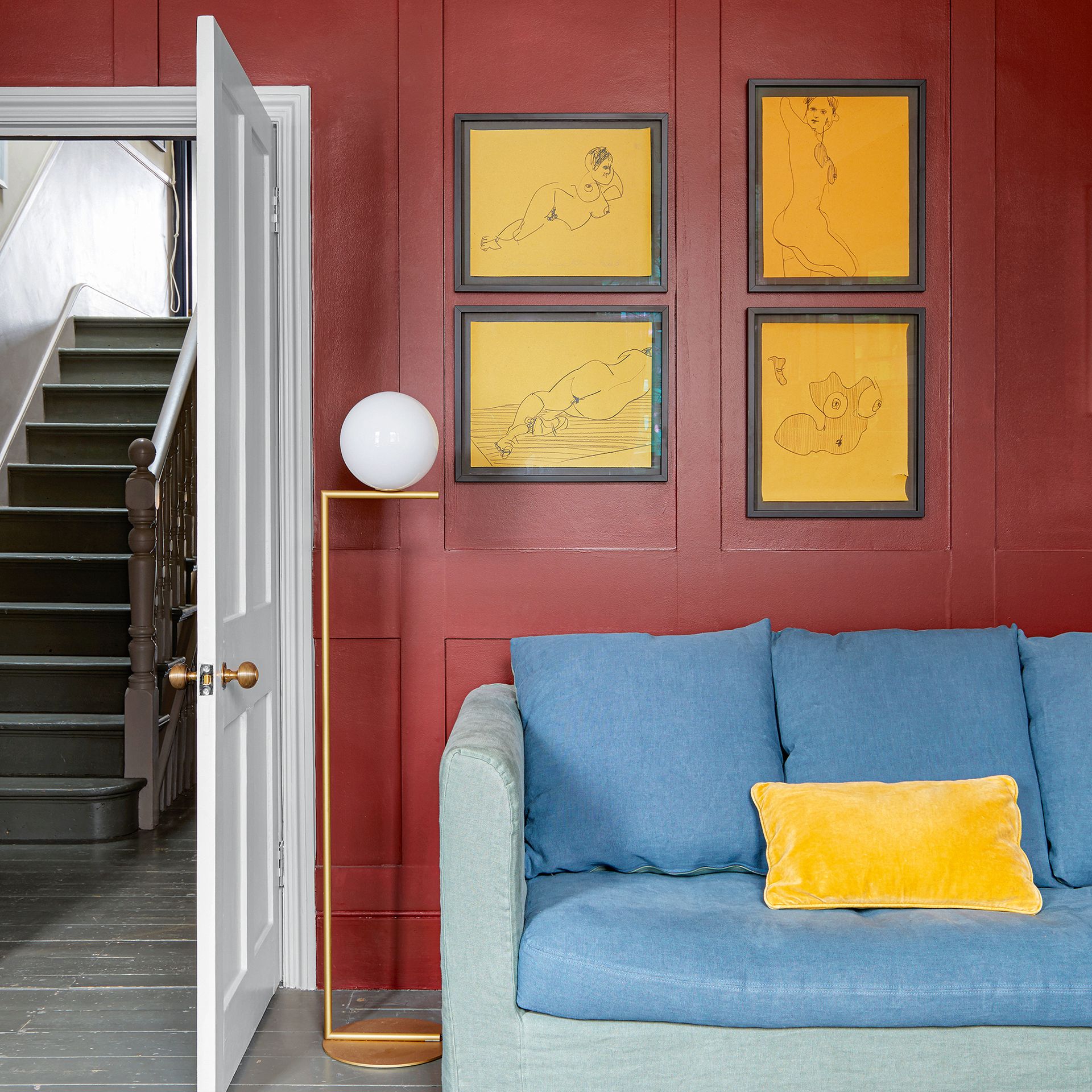 Living room with deep red panelled walls with artwork above blue sofa