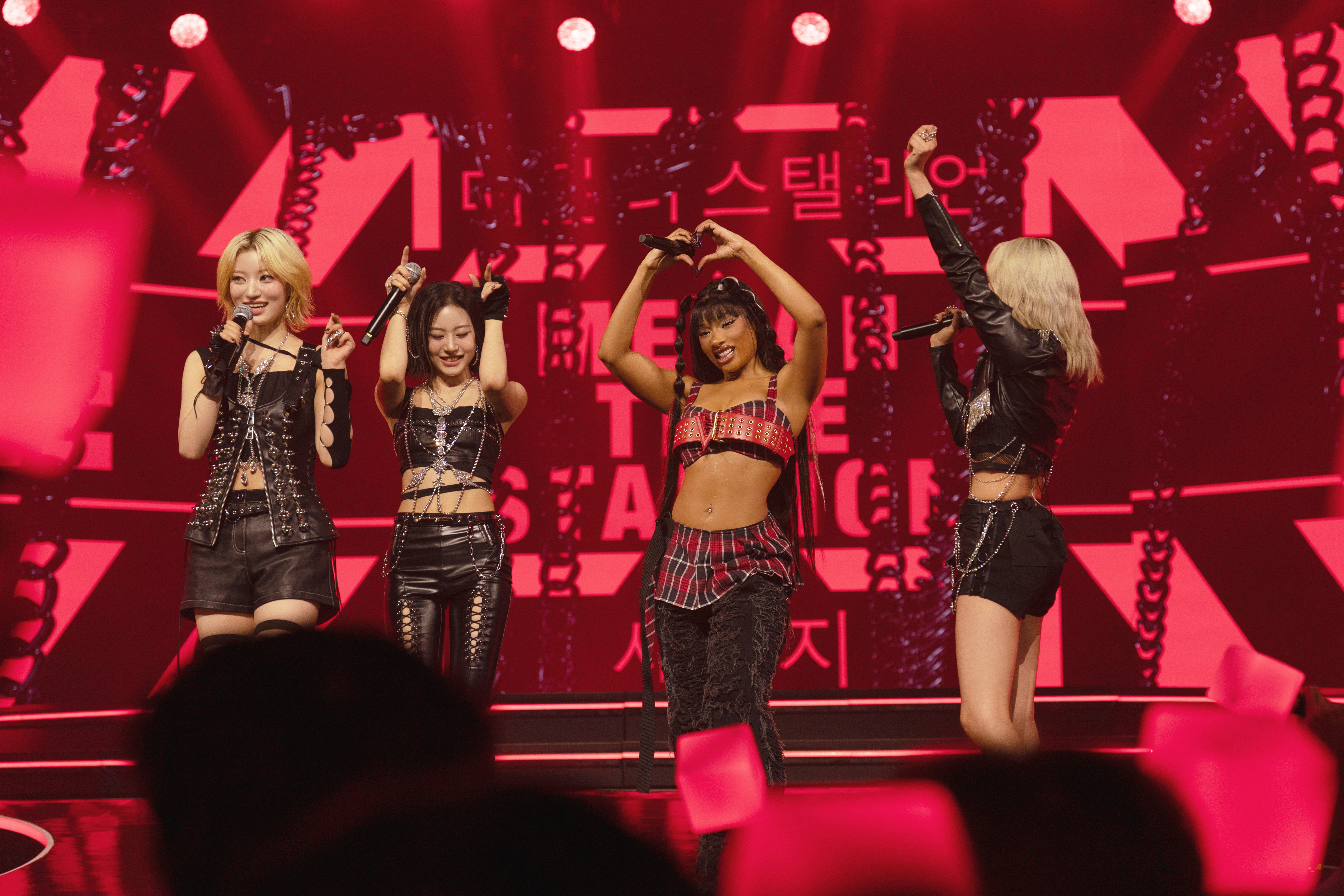 A group of women (l-r: Siyoon of Billlie, Sheon of Billlie, Megan Thee Stallion, and Moon Sua of Billlie) perform on a stage with Korean and English words behind them, in Apple TV+&#039;s &#039;KPOPPED.&#039;