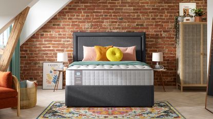 bedroom with a brick wall with a grey upholstered bed with a sealy mattress