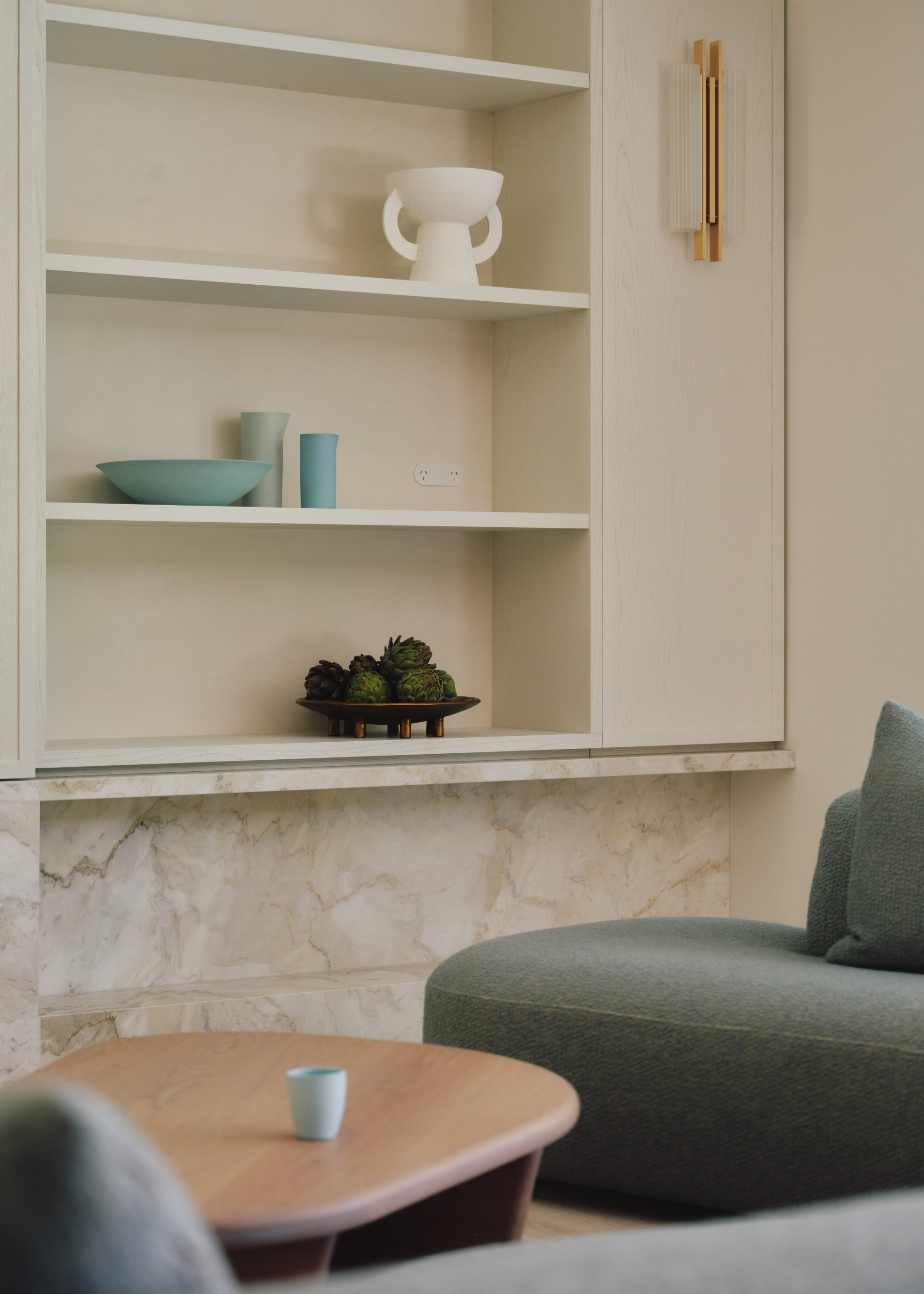 A living room shelving space with blue and white ceramics, a bowl of artichokes and a green sofa