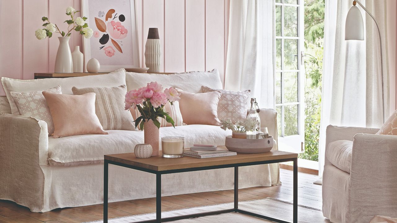 A wall-panelled pink-painted living room with a white skirted sofa and armchair