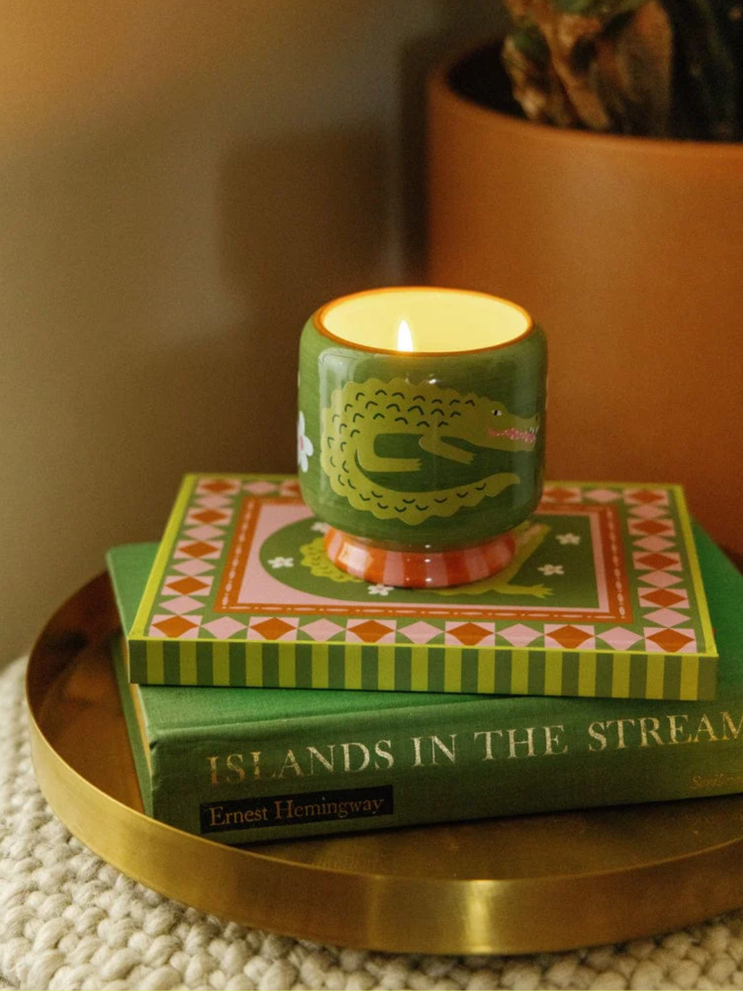 A green ceramic candle with a crocodile painted on the facade with a pear scent on a stack of books