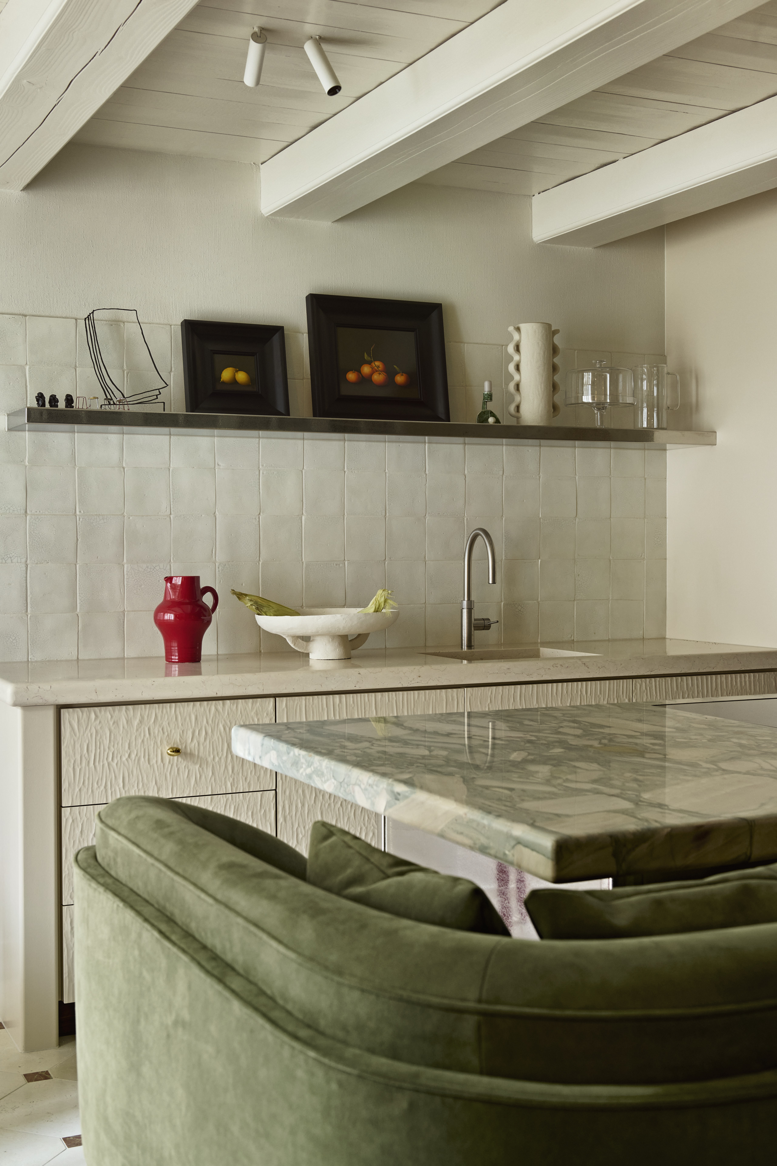 A green sofa around a kitchen island in a white and beige kitchen space