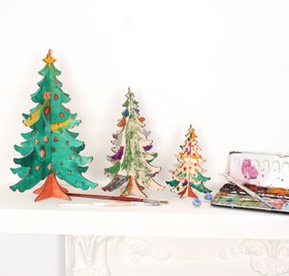 wooden Christmas trees painted by children on a white fireplace
