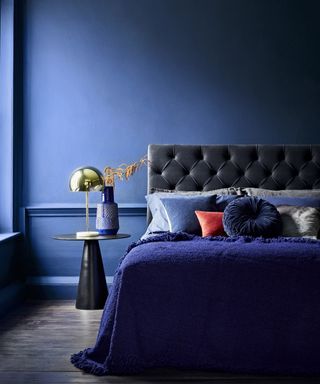 A dark blue bedroom with deep blue painted walls and a bed with blue velvet headboard.