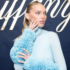 Elsa Hosk looks away from the camera with her hand on her face wearing a blue dress
