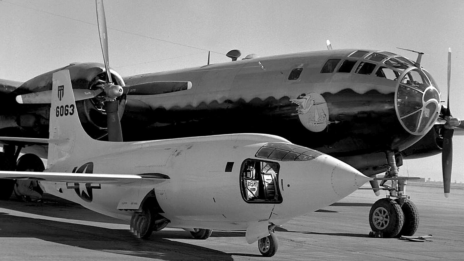 A small plane sits in front of a bigger, darker plane in a black and white photo.