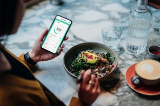 A woman looking at a calorie counting app on her phone while eating a salad