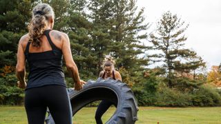 Two women flipping over tyre, doing CrossFit outside