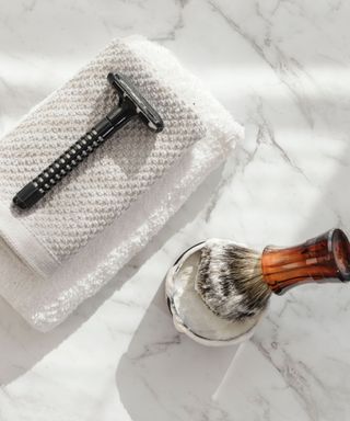 A razoe on a white washcloth next to a shaving brush