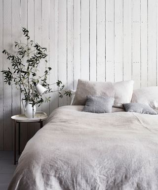 bed with grey bedding and a white shiplap wall