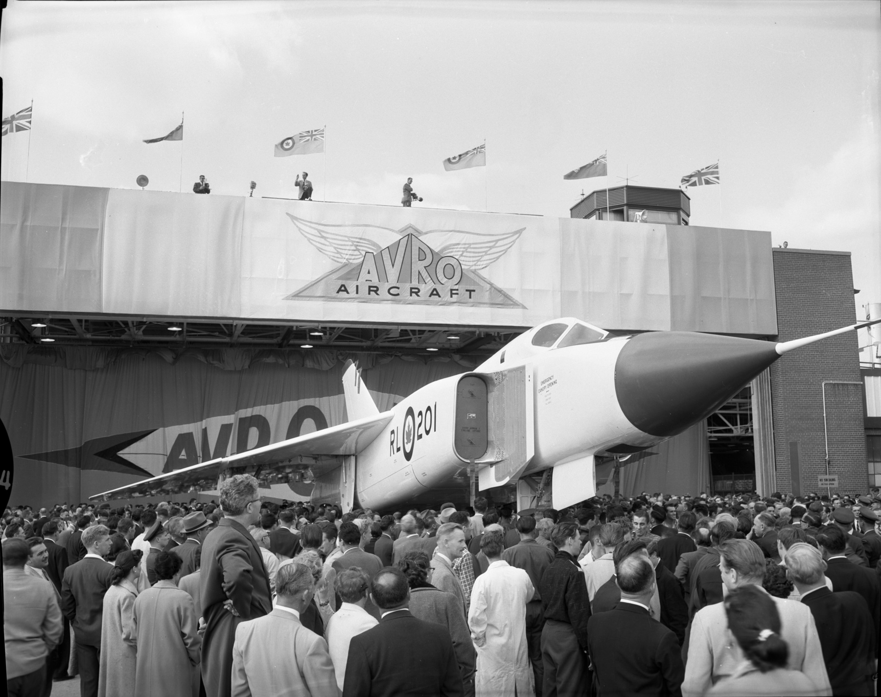 a jet plane with pointy nose in front of a large crowd of people. the photo is in black and white given the age