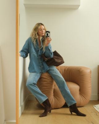 Anouk wears a denim shirt, jeans, brown suede boots, and a brown suede bag.