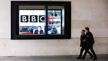 Pedestrians walking past a BBC screen