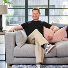 George Clarke in black t-shirt sitting on grey sofa from Sofology