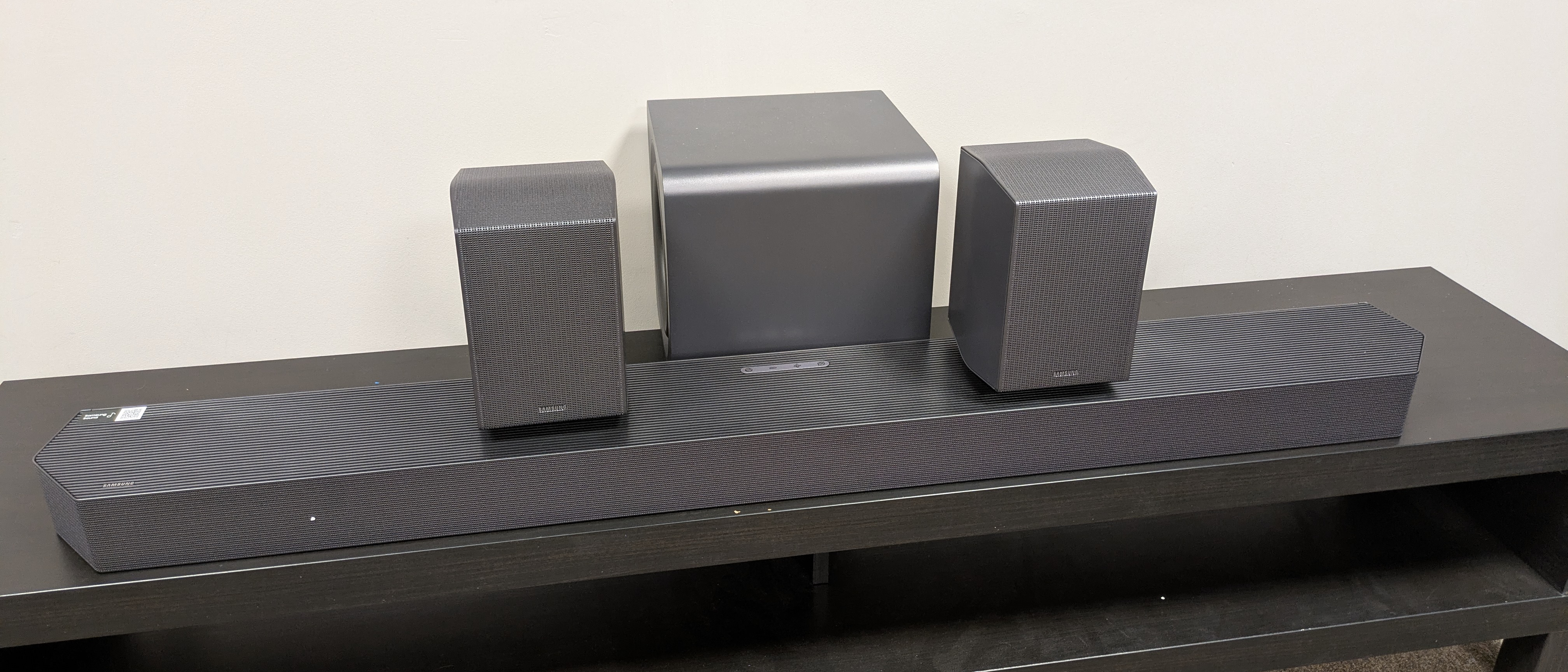 Samsung HW-Q990H soundbar on dark bench, showing main soundbar, subwoofer and two rear speakers 