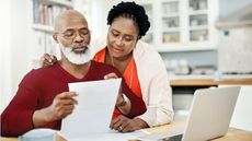 An older couple look over paperwork together while at the kitchen table.