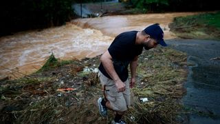 a bearded man in a dark blue cap and t shirt, tan shorts and sneakers walks away from the overflooded Turabo river on September 19, 2022 in Caguas, Puerto Rico