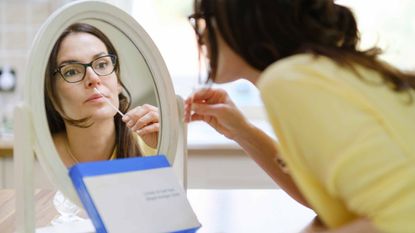picture of woman looking in a mirror while using a home COVID-19 test kit