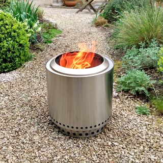 The stainless steel Solo Stove Ranger fire pit with flames burning in a gravel garden