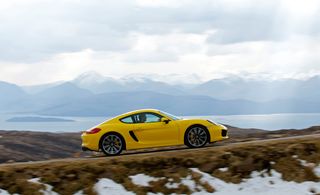 Action shot of a yellow sports car driving uphill with water and mountains in the background