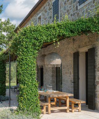 stone house with terrace with pergola with wooden dining table and benches and rattan lampshades