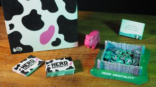 The Herd Mentality box, cards, tokens, and pink cow on a wooden table