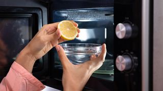 Person placing lemon and a bowl of hot water into a microwave.