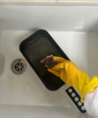 Person cleaning air fryer with tea bag and yellow gloves