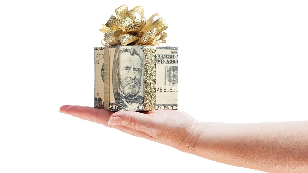 A gift box wrapped in a fifty-dollar bill with a bow sits on a woman&#039;s palm.