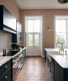 The Real Shaker Kitchen by deVOL with peachy pink walls, wooden flooring, dark blue cabinetry, marble countertops and brass accents