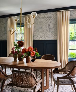 Dining room with oval wooden table, flowers, dining chairs, cream curtains, blue walls with wallpaper
