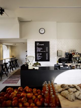 SIS Deli & Cafe, Finland. A deli with a black serving counter, tables against the wall and shelves with produce on them.
