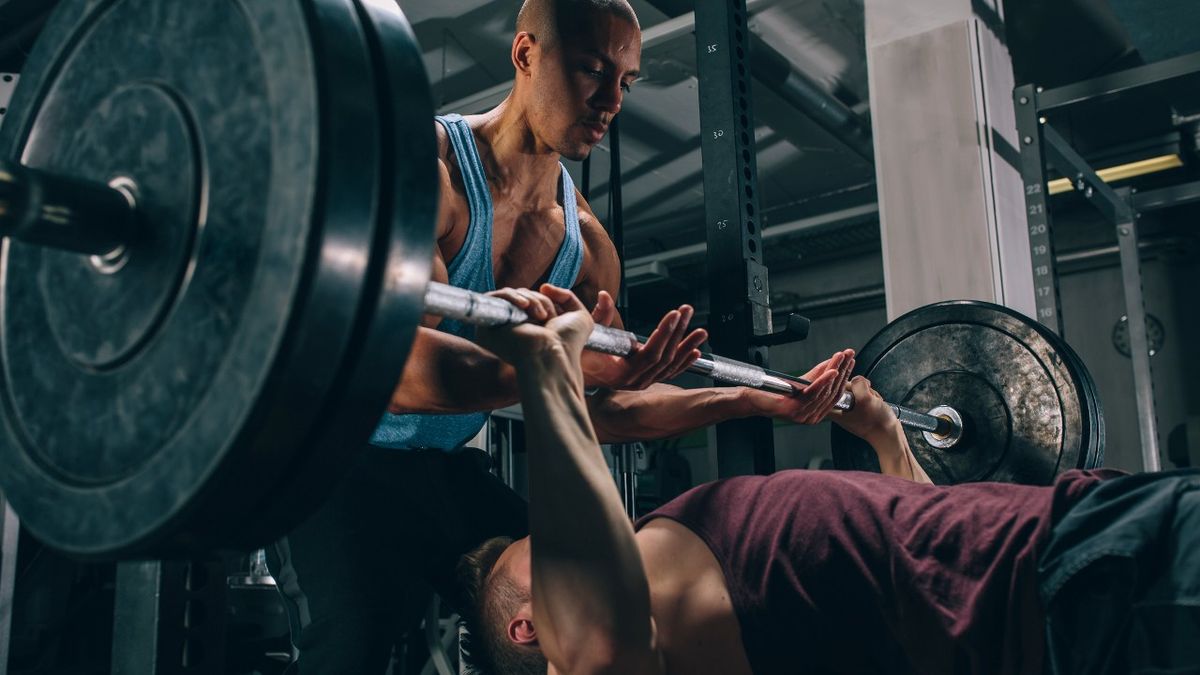 Man presses heavy barbell with spotter