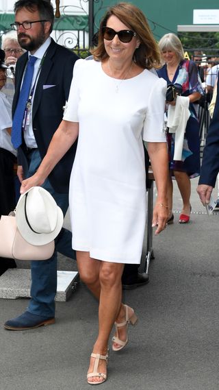 Carole Middleton attends Wimbledon on July 03, 2019 holding a hat and wearing a white dress and pink-beige sandals