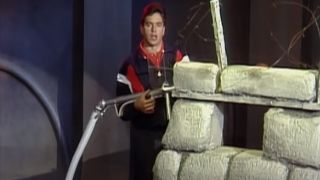 A host showing off the old Assault course in American Gladiators S1 E1.