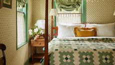 floral wallpapered hotel room with wooden four poster bed styled with bed bed sheets and a green patchwork scandinavian style floral quilt with a yellow ruffled pillow