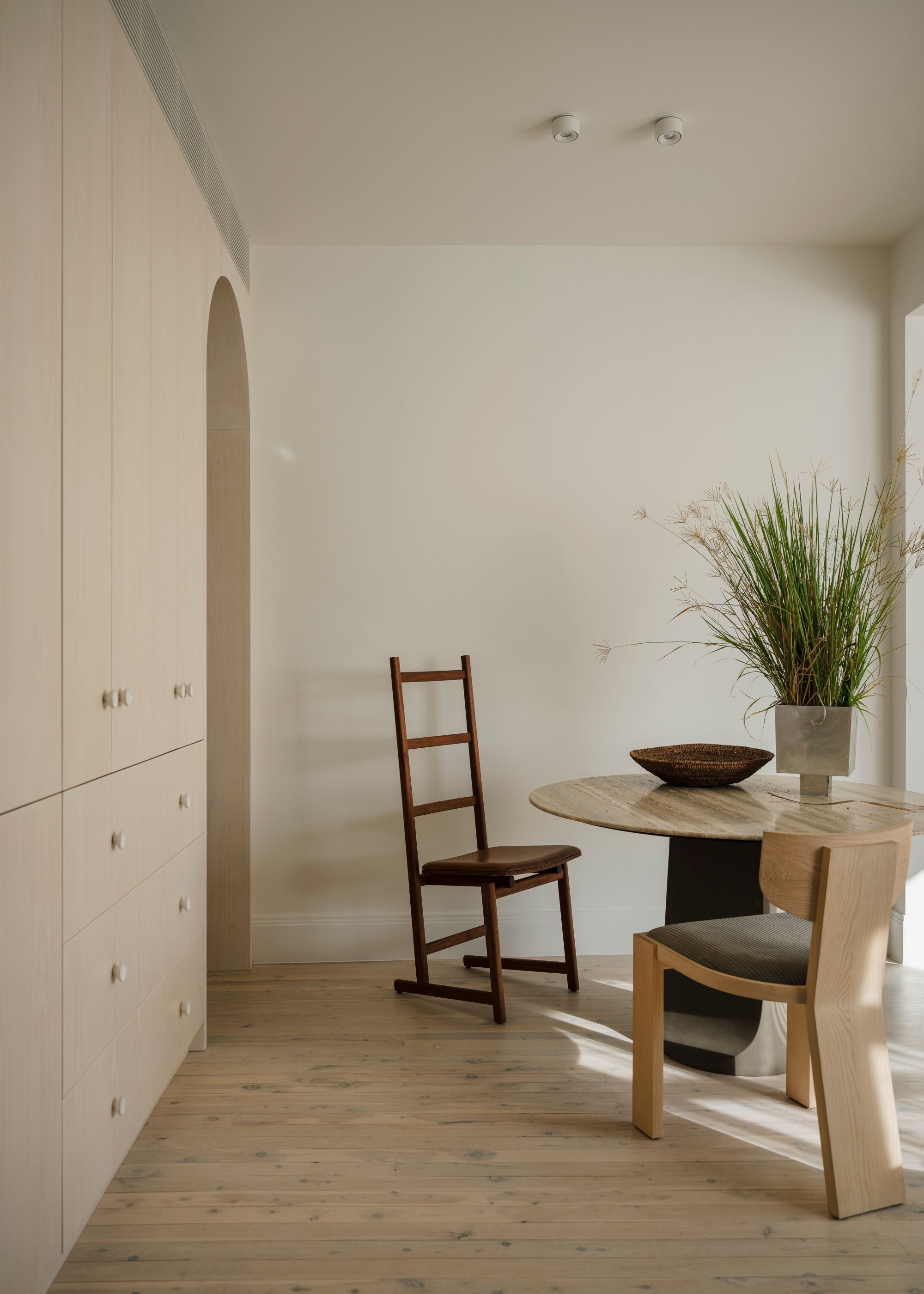 A dining room with minimalist cabinetry, mismatched dining chairs, a potted plant and a bowl