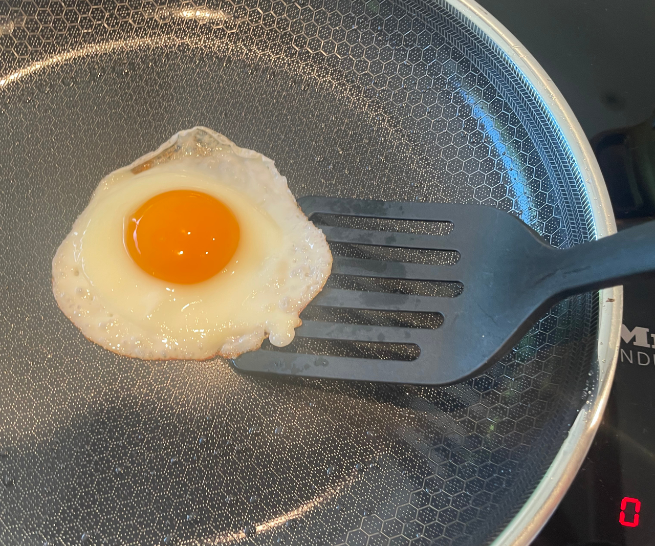 Someone using a black plastic spatula to flip a fried egg in a pan