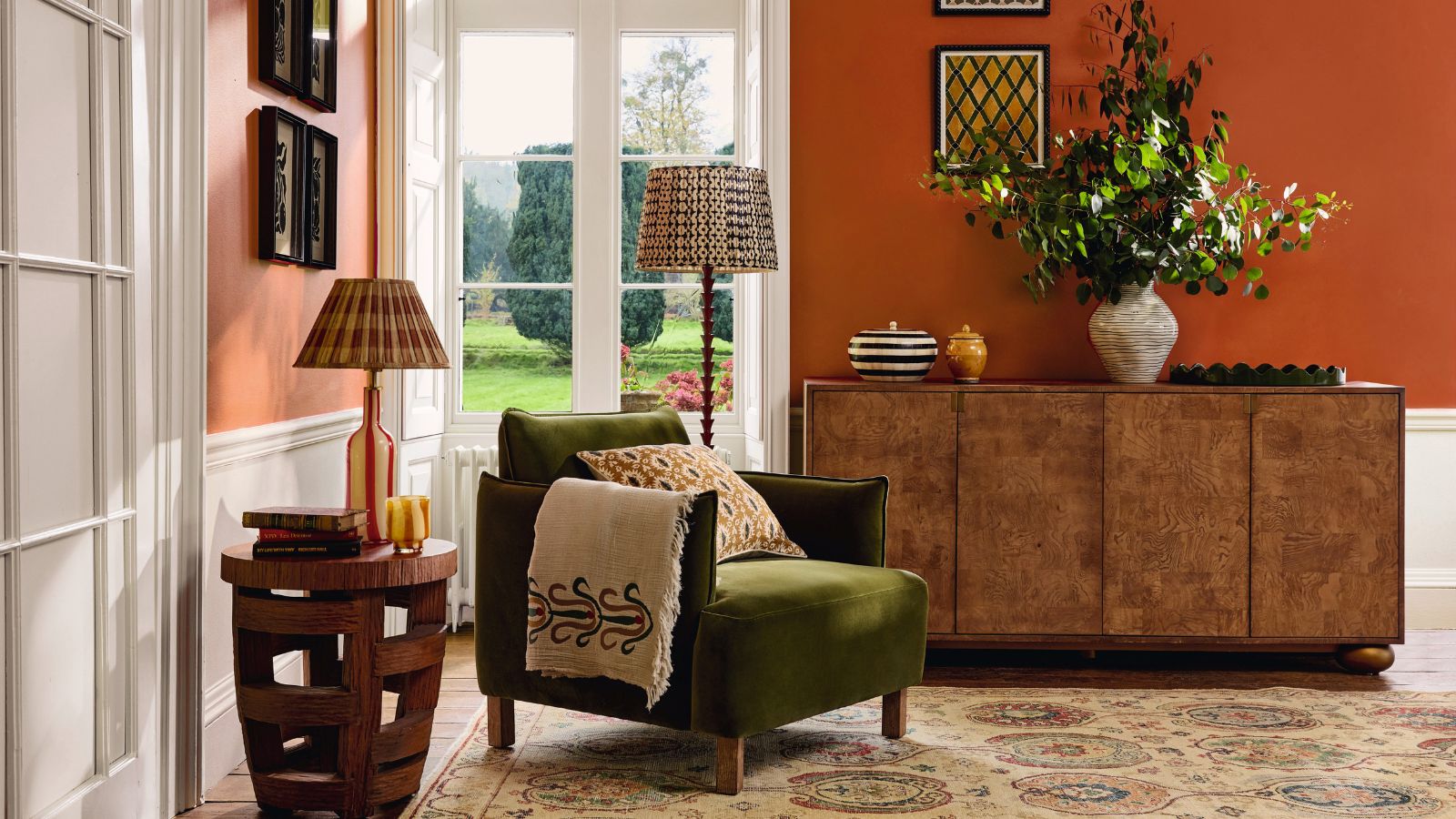An orange painted living room with a green arm chair, and a wooden side board