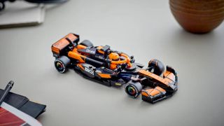 Lego McLaren car set on a gray surface, with a pen and plant pot in the background