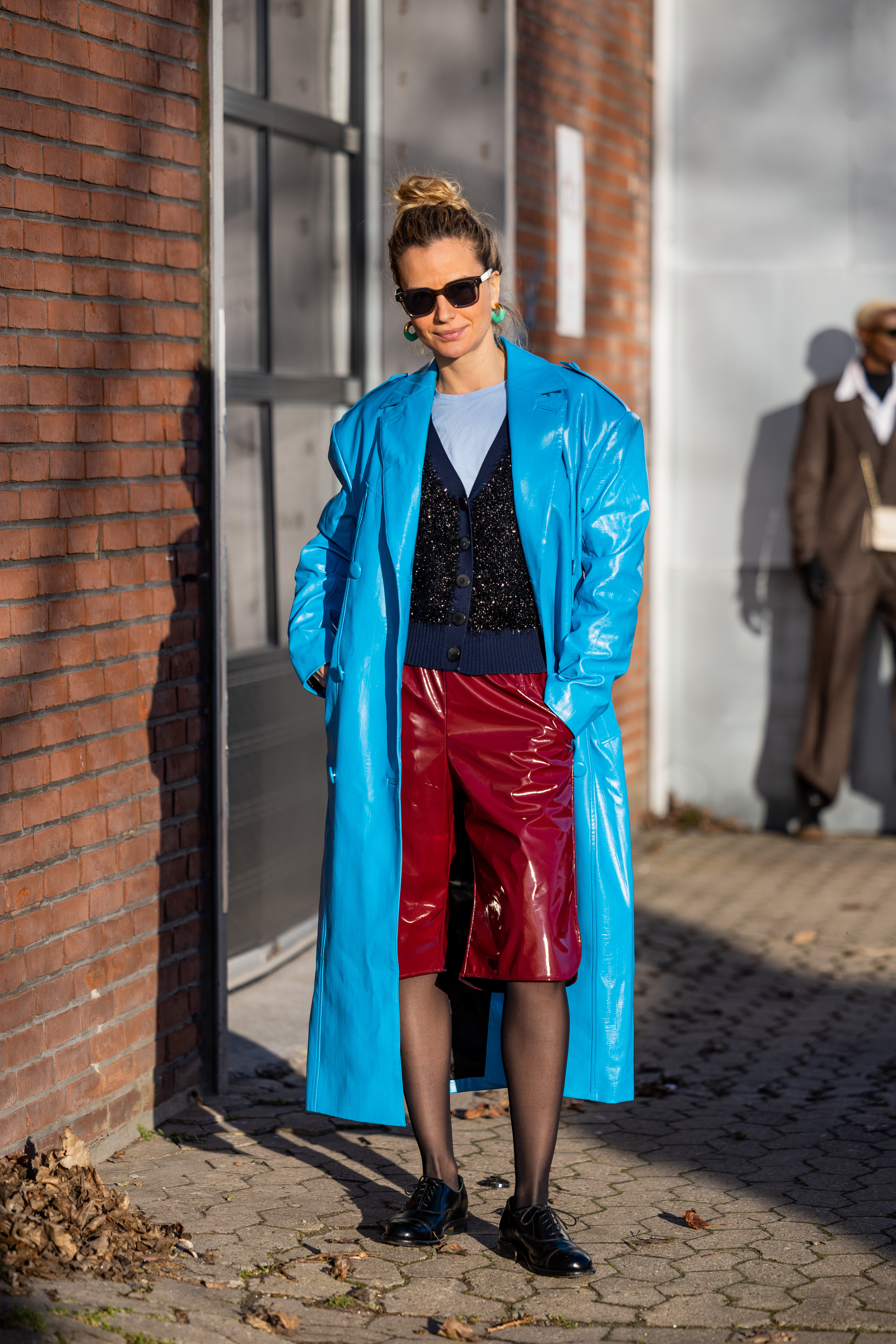COPENHAGEN, DENMARK - FEBRUARY 02: Mija Knezevic wears blue varnished shiny coat, red shorts, tights, navy cardigan outside Holzweiler during the Copenhagen Fashion Week Autumn/Winter 2023 on February 02, 2023 in Copenhagen, Denmark. (Photo by Christian Vierig/Getty Images)