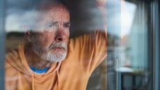 Mature man looking through window with worried expression 