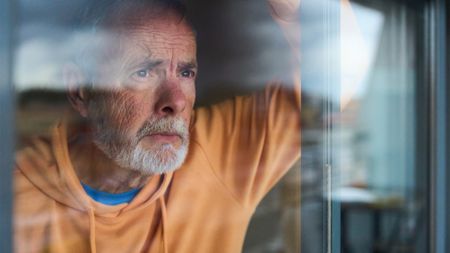 Mature man looking through window with worried expression 