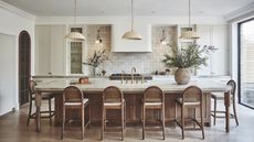A kitchen with a large marble island with a fluted edge, a wall of cream zellige tiles, and wooden herringbone flooring