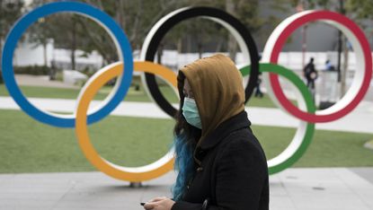 A woman wearing a face mask walks past the Olympic rings in Tokyo